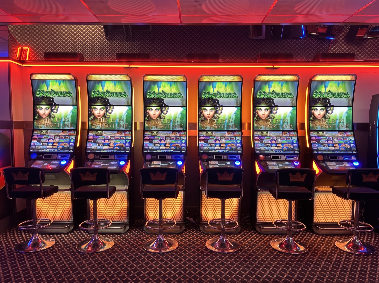 Inside Richmond Leisure — a row of six identical Medusa machines with glowing honeycomb bases and a stool at every one, under the red neon.